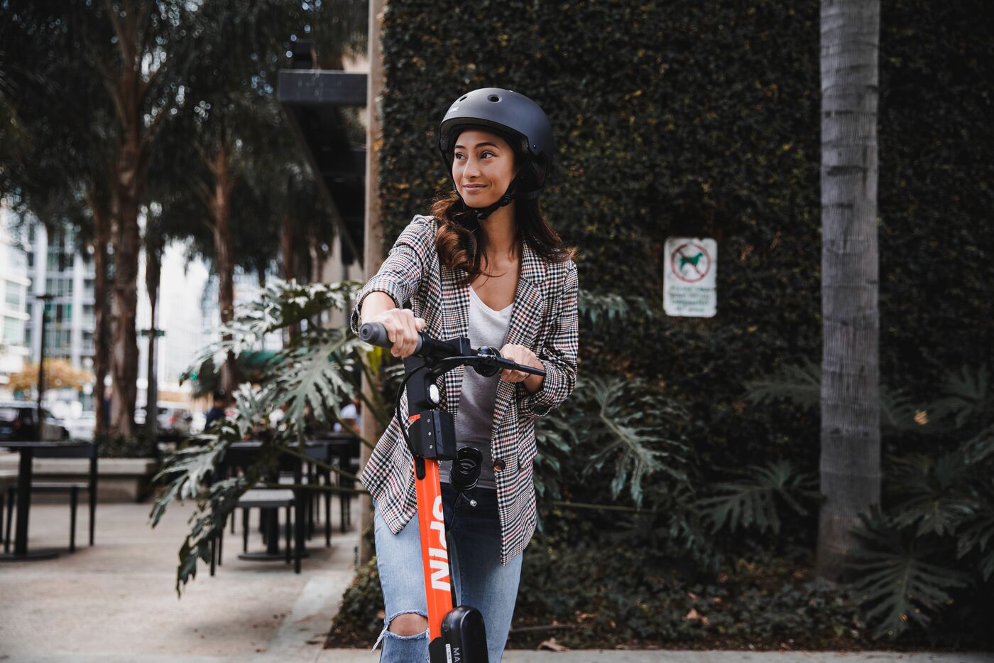 A rider in a helmet with an orange Spin scooter on a city sidewalk