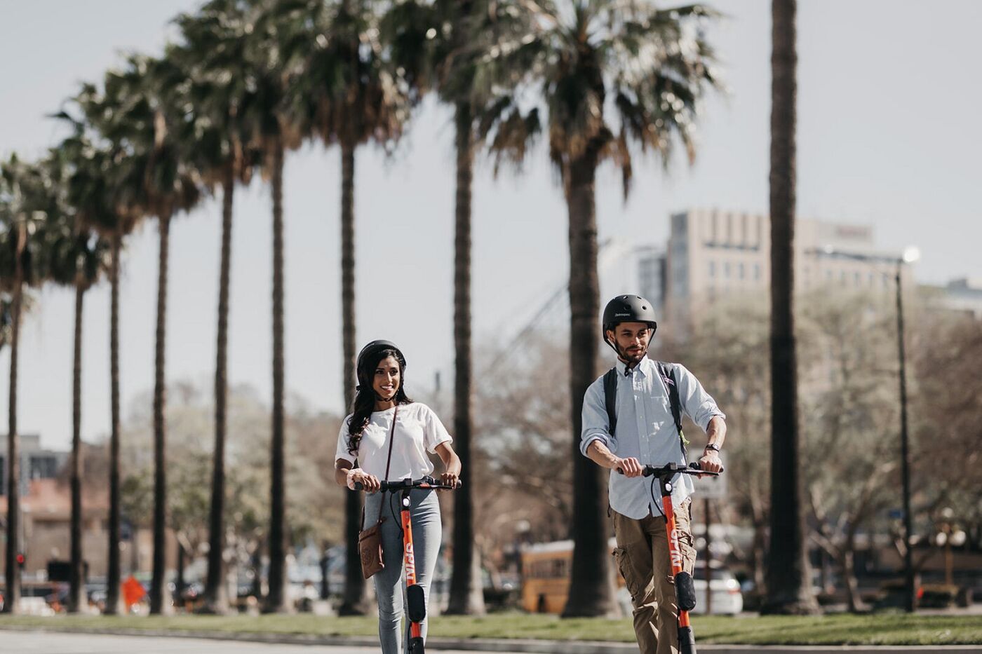 Two riders on orange Spin scooters down a palm-lined street