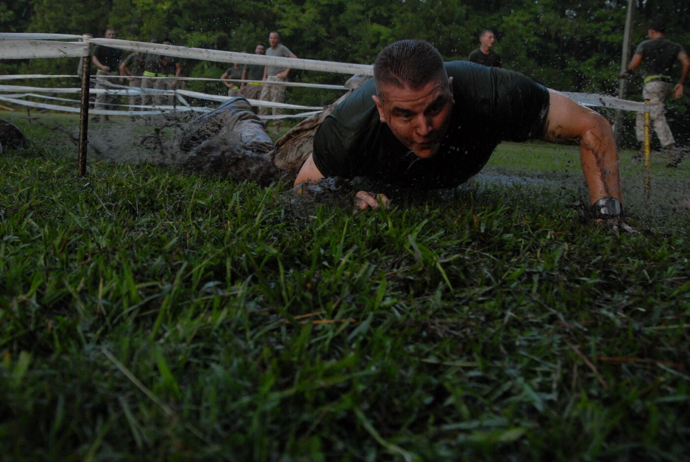 A mud-splattered Marine low-crawling under a rope obstacle at dawn